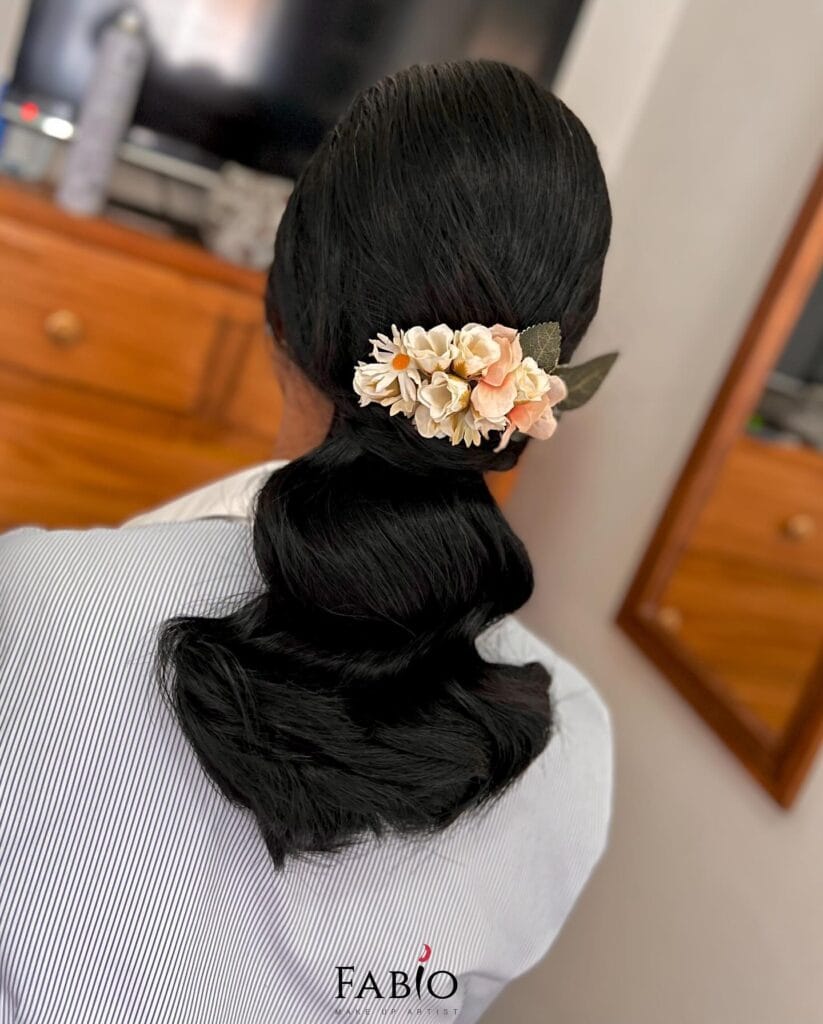 A woman with long black hair styled in a low bubble ponytail, adorned with a delicate peach and white floral hair clip.