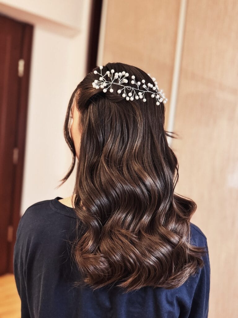 A rear view of long, chocolate brown hair styled in voluminous, glossy waves with a decorative pearl hairpiece across the back.