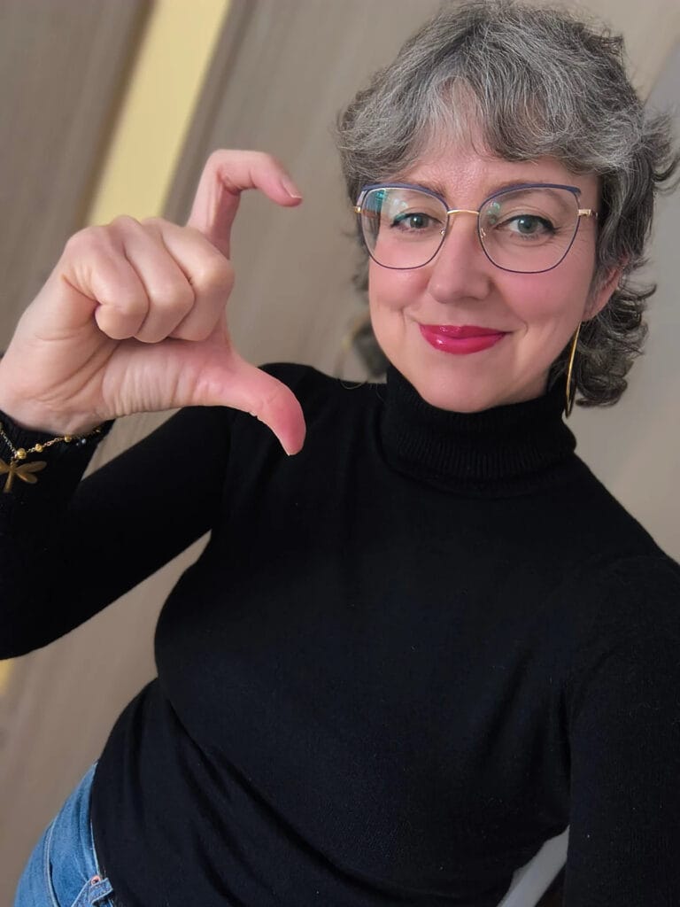 A woman with short, curly salt-and-pepper hair and soft bangs wearing glasses.