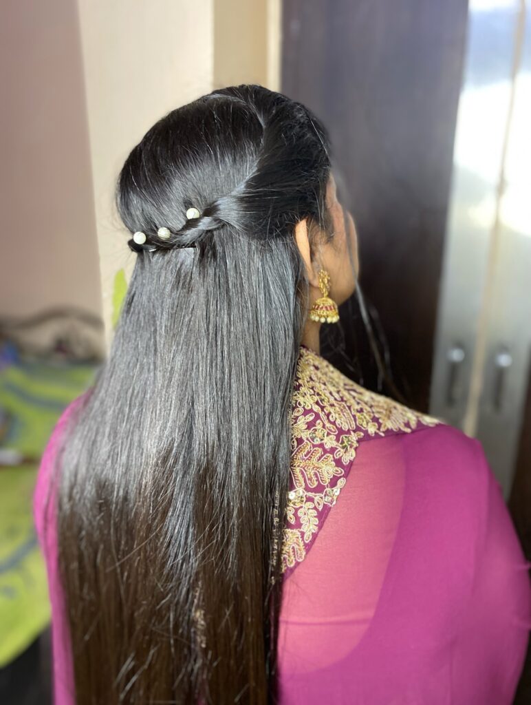 A woman from behind shows long, straight black hair in a half-up twisted style decorated with small pearl pins.