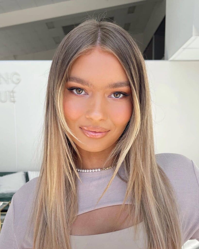 A woman with long, straight blonde and light brown hair featuring bright, face-framing highlights and a center part.