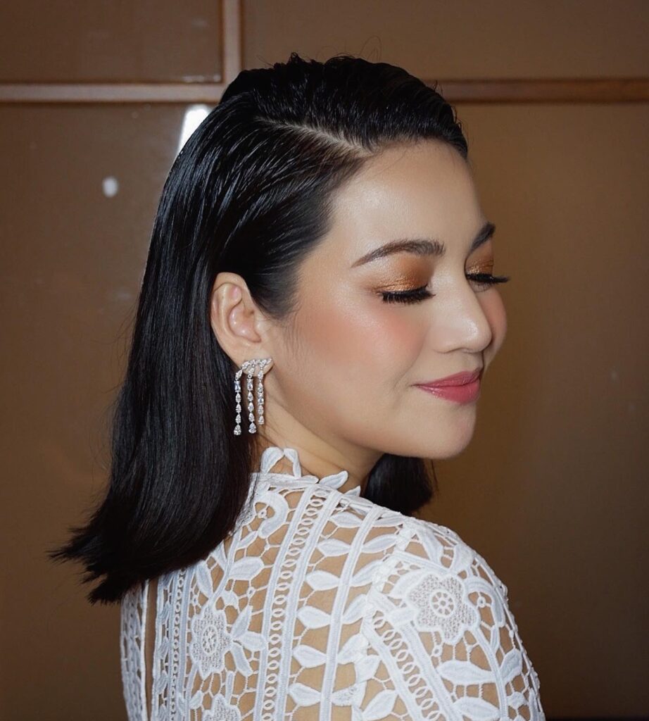 A woman with shoulder-length black hair styled in a sleek, wet look with a deep side part and the sides tucked back.