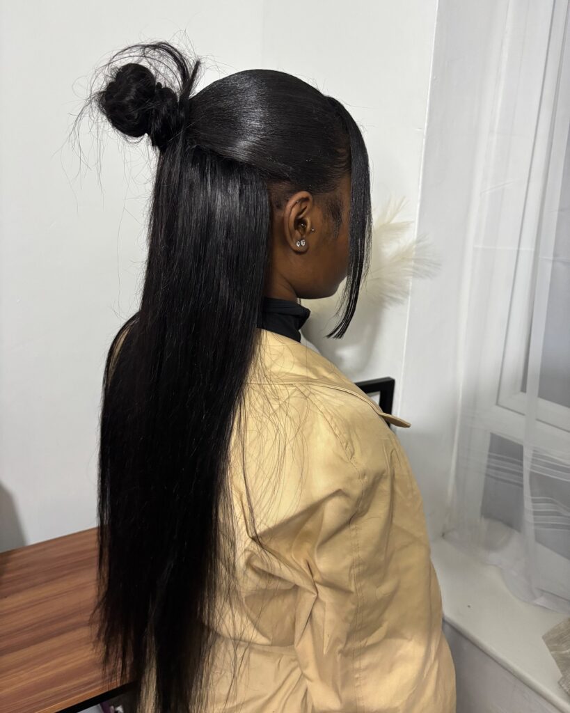 A woman in profile with long, sleek black hair styled in a half-up topknot with long face-framing strands.