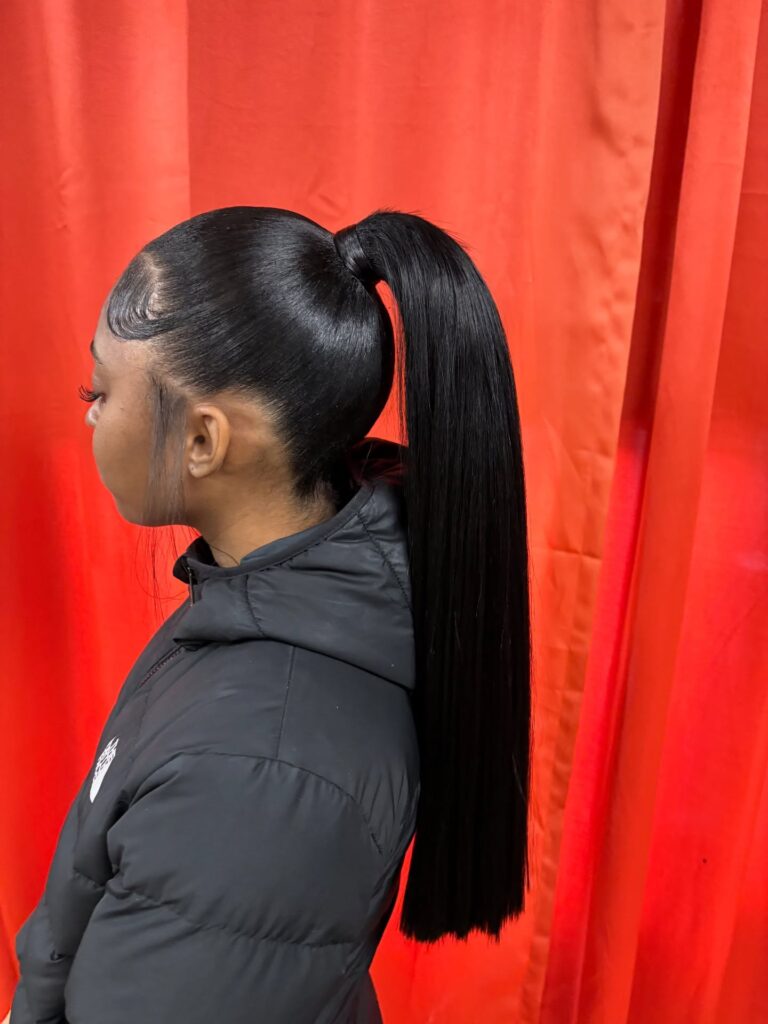 A woman in profile with a high and sleek black ponytail featuring perfectly laid edges and pin-straight hair.