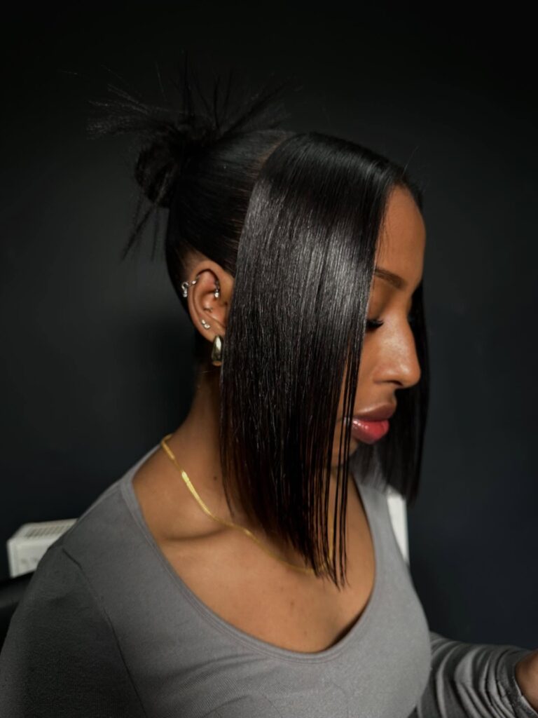 A woman in profile with a sleek black updo featuring long straight side bangs and a spiky textured bun.