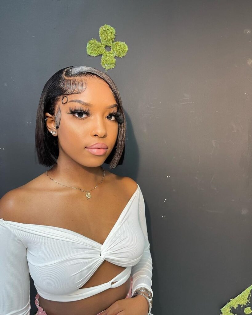 A woman with a sleek chin-length blunt bob in a dark brown shade featuring a deep side part and styled edges.