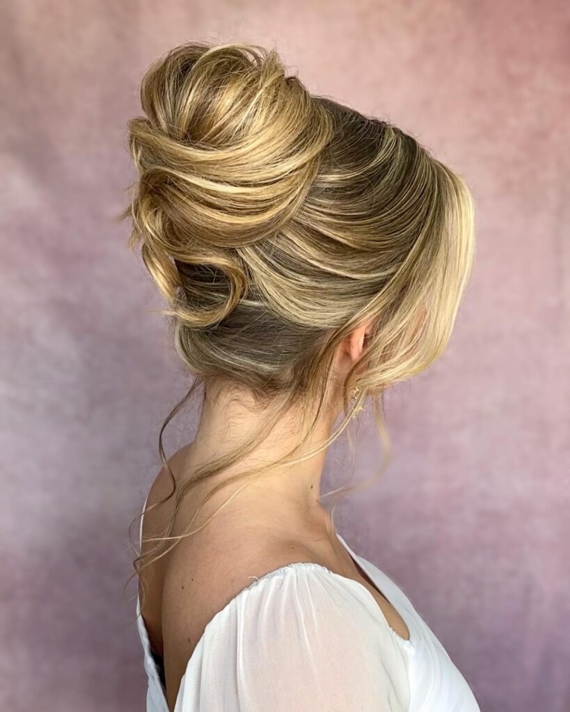 A side profile view shows a woman with blonde highlighted hair styled in a high, voluminous French twist with loose curling strands at the neck.