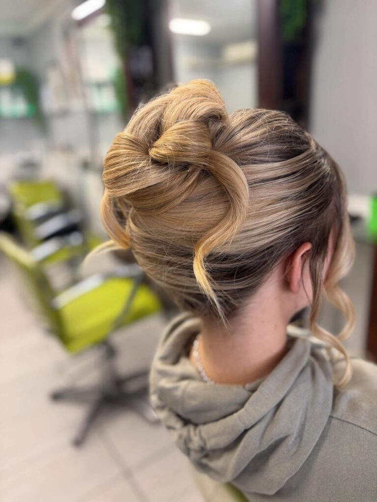 A woman with ash blonde highlights shows off a modern French twist with a distinct knotted finish and soft face-framing curls.