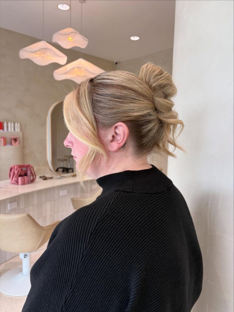 A side profile of a woman with short blonde hair featuring a textured French twist and long side-swept bangs.