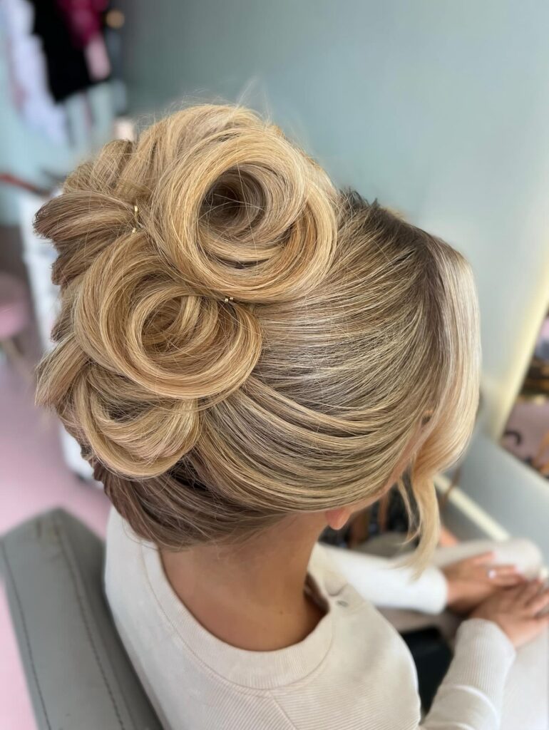 A top-down view shows a woman with blonde hair styled in a French twist that features several large and soft hair swirls pinned to the top of her head.