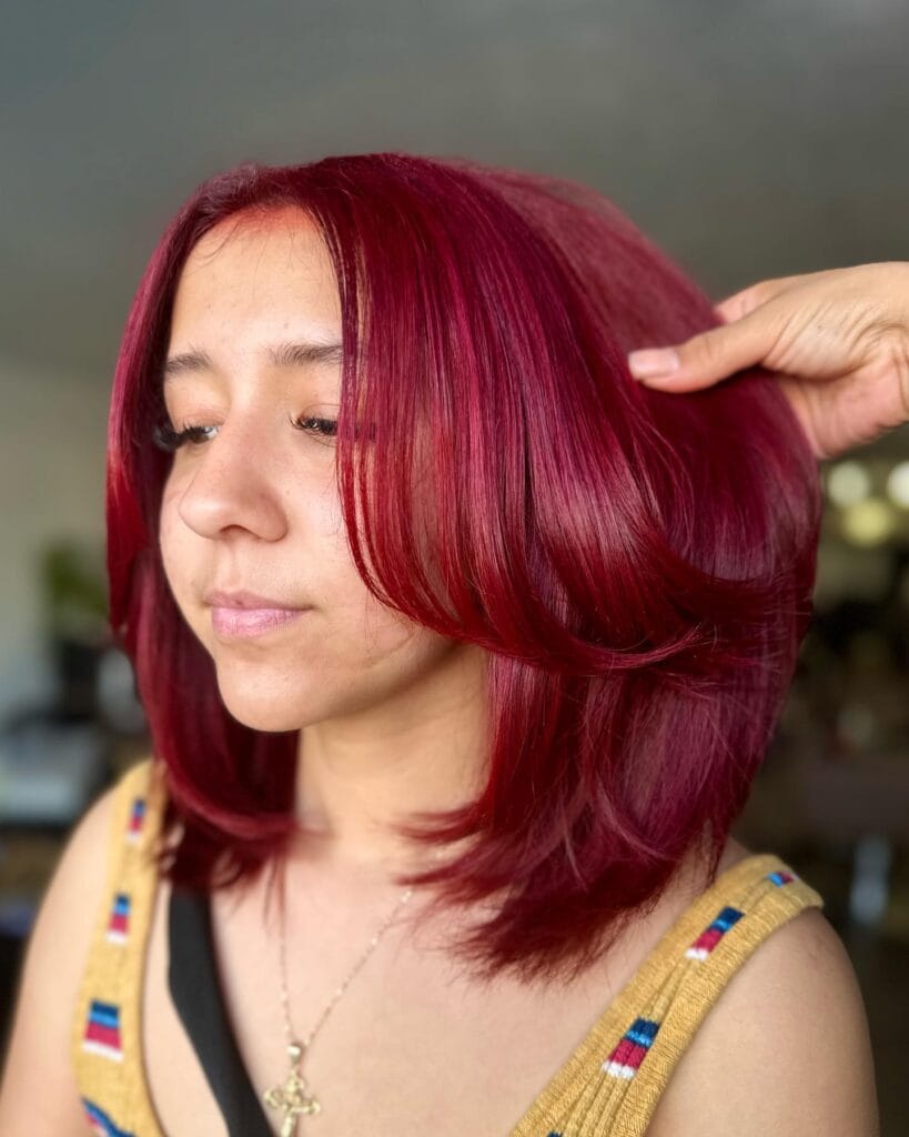 A young woman with a medium-length bob styled in soft, subtle layers and colored a vibrant raspberry red.
