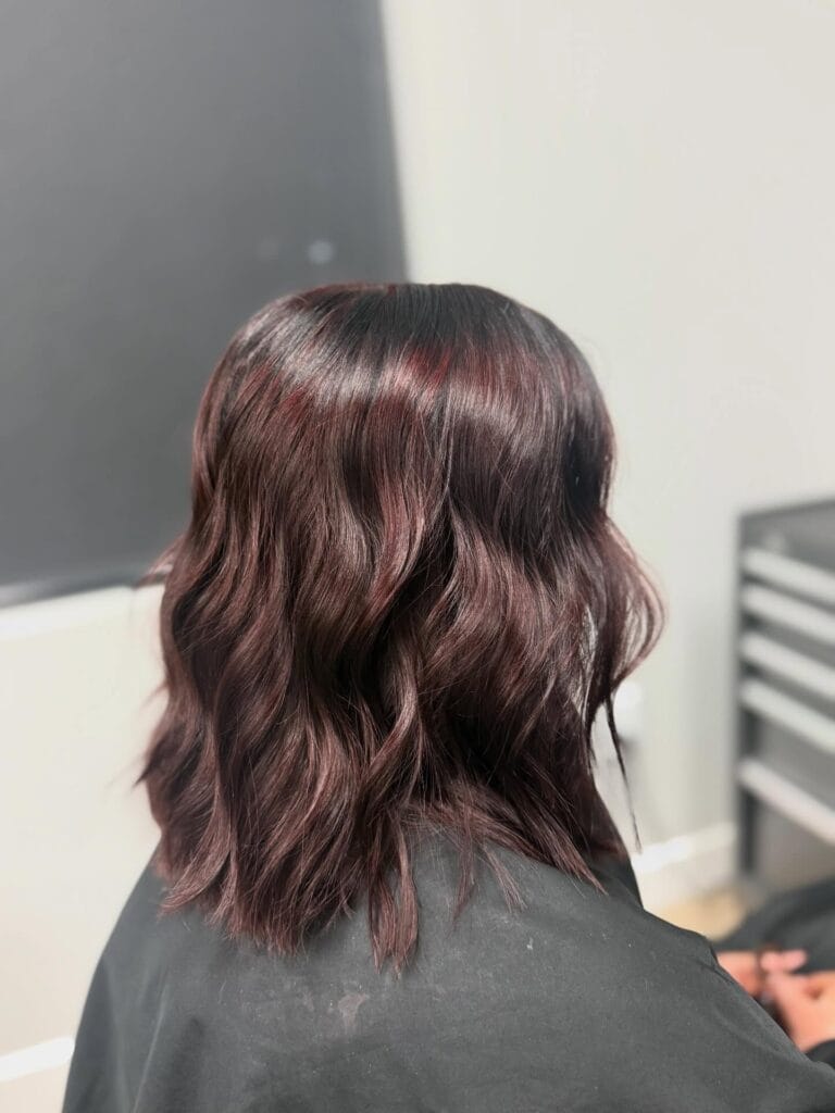 A back view of a woman with medium-length wavy hair in a dark mahogany-red shade.