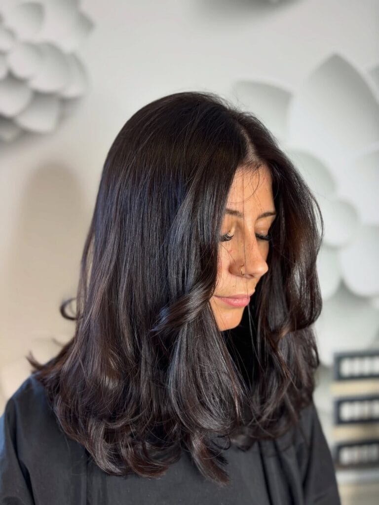 A woman with glossy dark brown medium-length hair styled with bouncy layers and outward-curled ends.