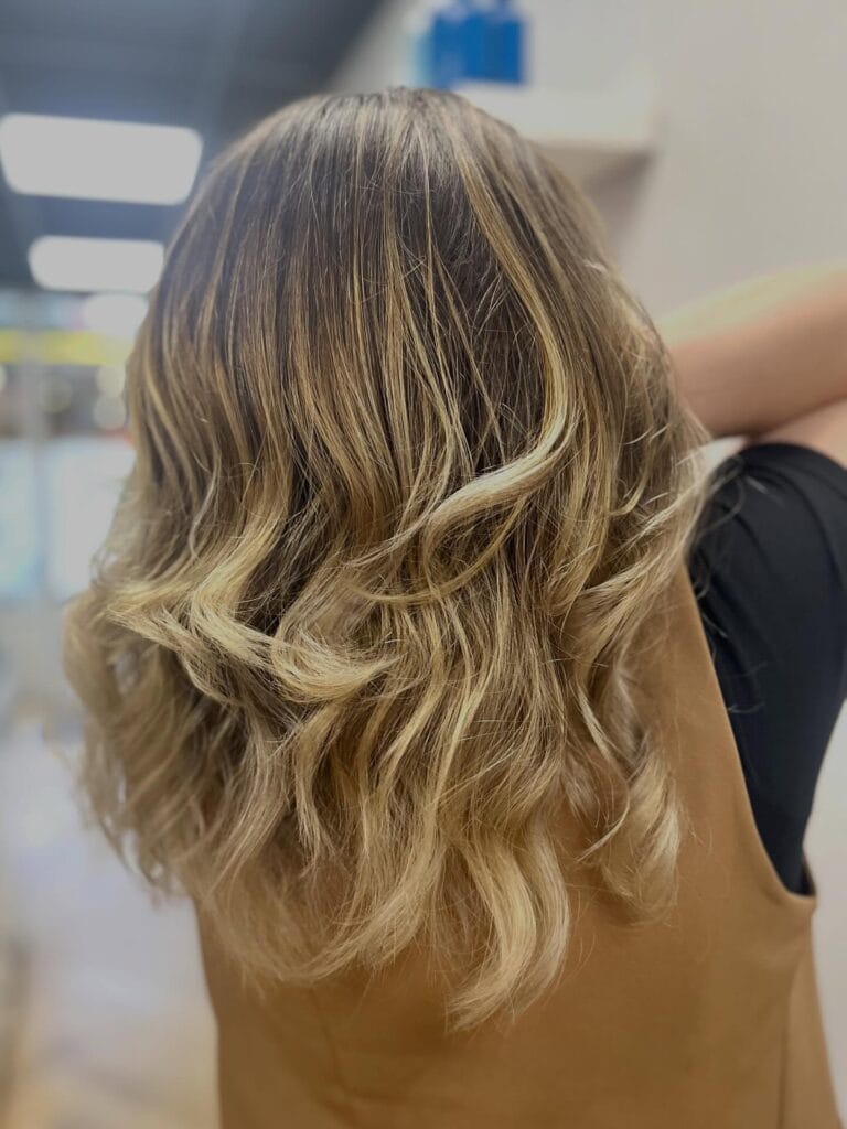 A back view of a woman with medium-length curly hair featuring a golden blonde and brown balayage.