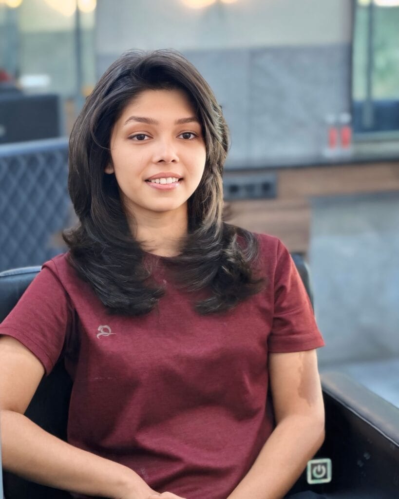 A young woman with voluminous medium-length dark hair featuring layered face-framing pieces and a side part.