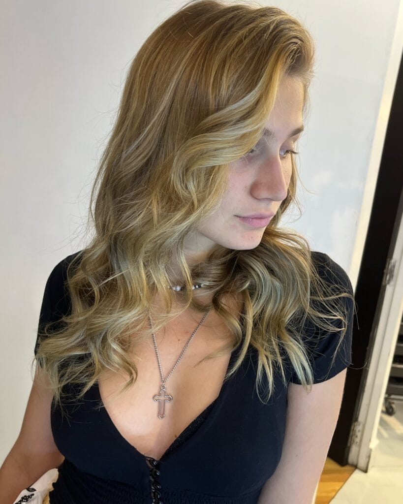 A young woman with medium-length sandy blonde hair styled in loose beachy waves with sun-kissed highlights.