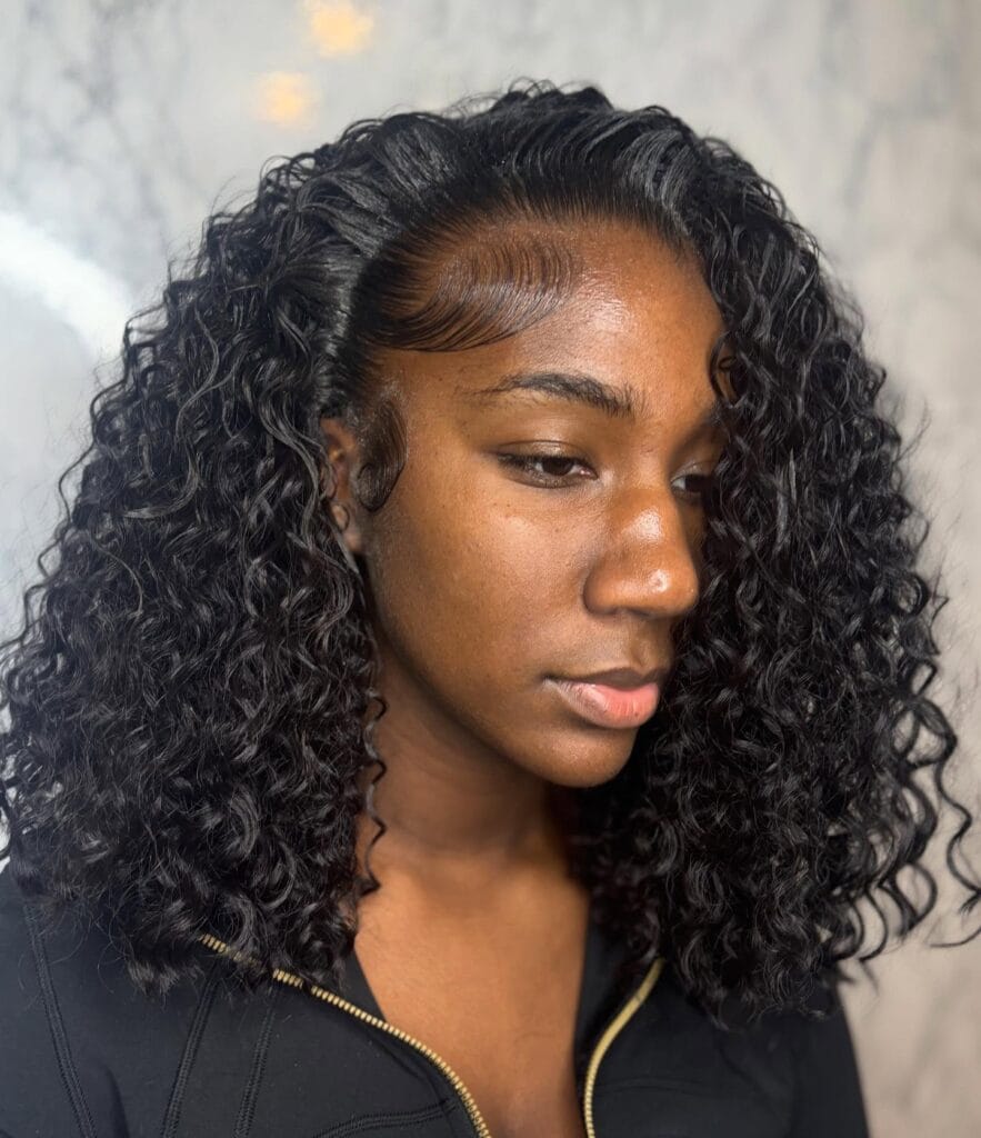 A young woman with medium-length voluminous black curls and perfectly styled edges.