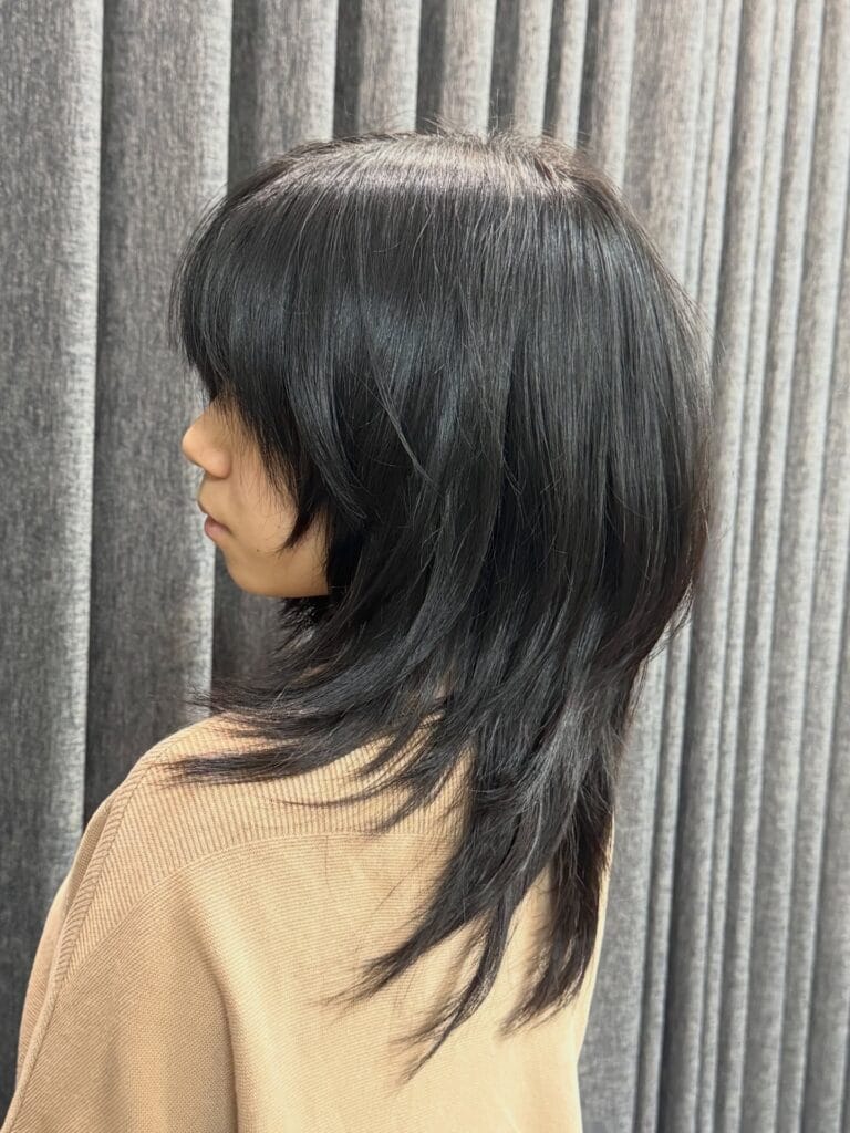 A side profile of a woman with a layered jet black shag hairstyle featuring a full fringe and feathered ends.