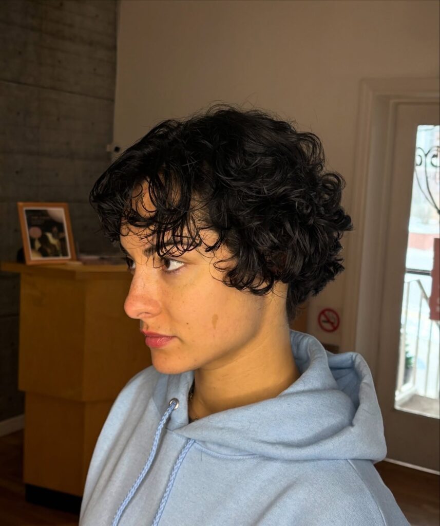 A woman in profile wearing a dark textured pixie shag with short piecey waves and a soft fringe.
