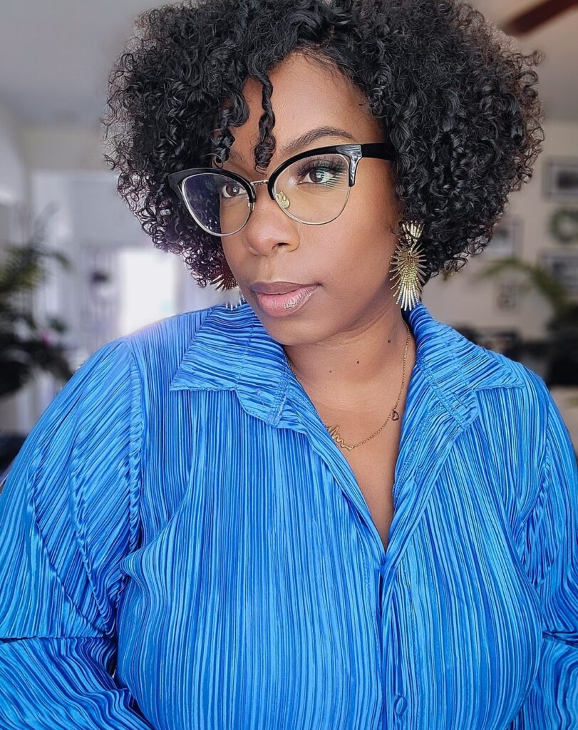 A woman with a voluminous, rounded black coily bob and a few curls falling over her forehead.
