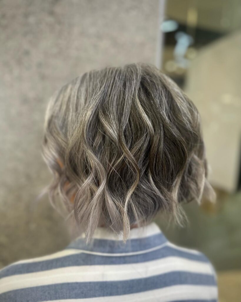 A view from behind of a woman with a chin-length silver ash bob featuring loose textured waves.