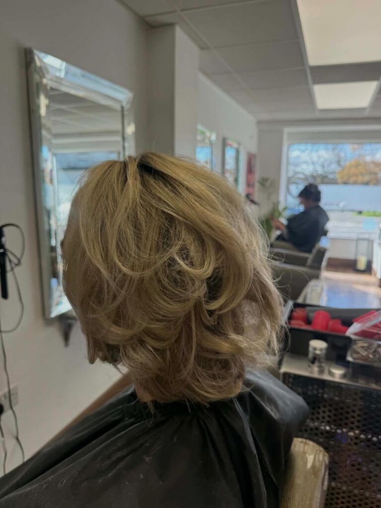 A medium-length hairstyle with voluminous choppy layers and warm blonde tones is shown from the back.