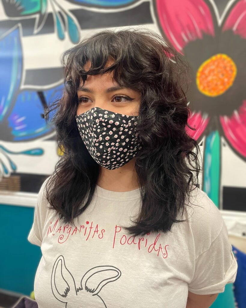 A woman with a medium-length dark shaggy wolf cut featuring voluminous choppy layers and full bangs.