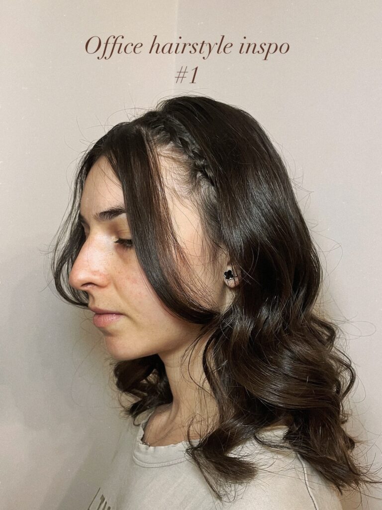 A side profile of a woman with medium-length dark brunette wavy hair featuring a small braid used as a headband and loose front pieces.