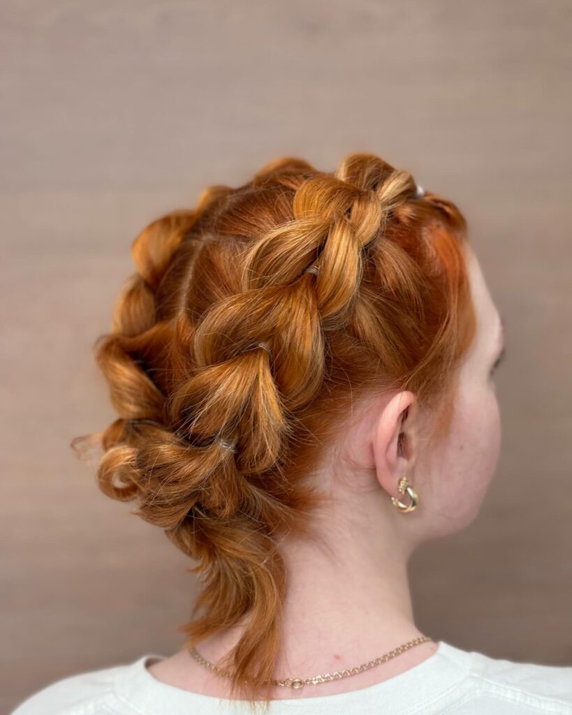 A woman with vibrant copper red hair viewed from the back showing off a voluminous pull through braid secured with small clear elastics.