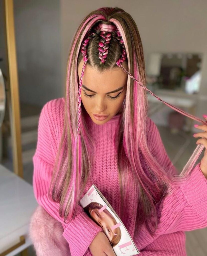 A woman from above, wearing a bright pink knit sweater, shows off her long blonde and brown hair with vibrant pink streaks styled in a sleek, half-up braided ponytail with braided side tendrils.