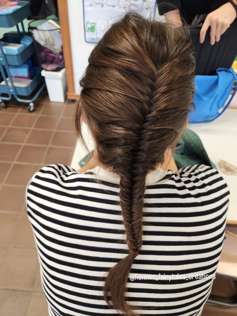A woman from behind wearing a black and white striped shirt with her long brown hair styled in a tight French fishtail braid.
