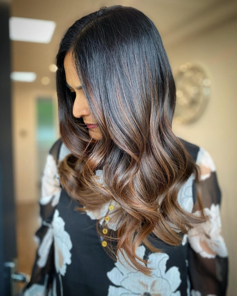 Medium to long wavy hair with a warm ombre blend from dark to light.