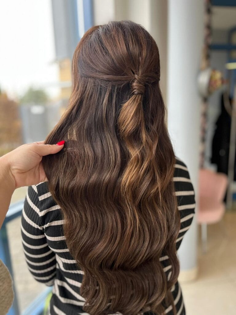 Long wavy brunette hair styled half up with a wrapped section at the back.