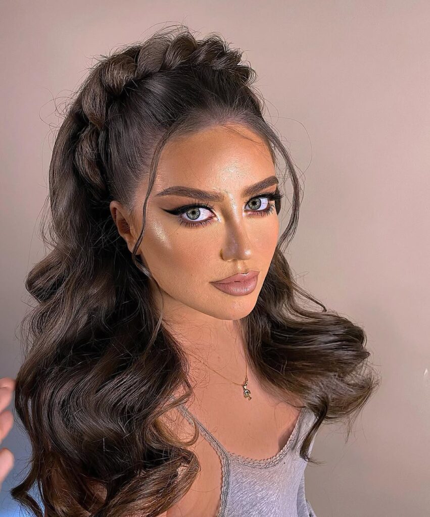 Long dark brown wavy hair with a voluminous half-up style and braided crown detail.