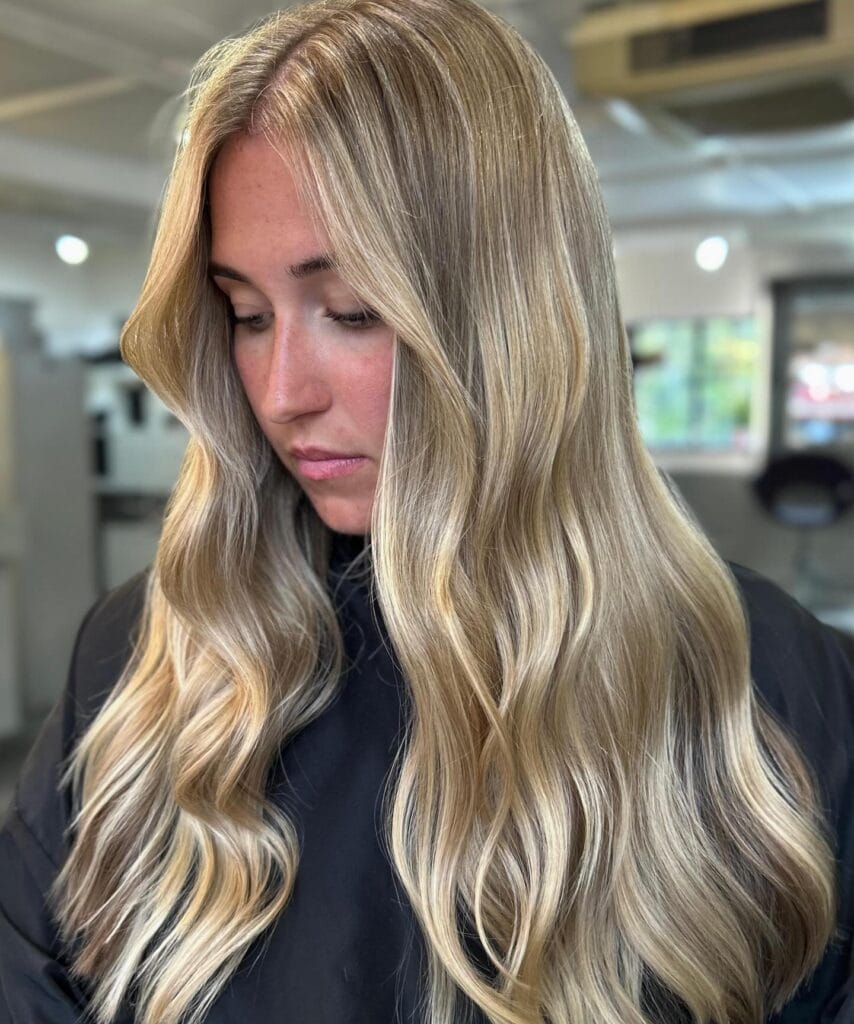 A woman with long wavy blonde hair featuring face-framing highlights and subtle layers.