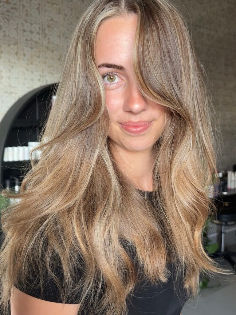 A woman with long layered ash blonde hair featuring bright face framing highlights and soft waves.