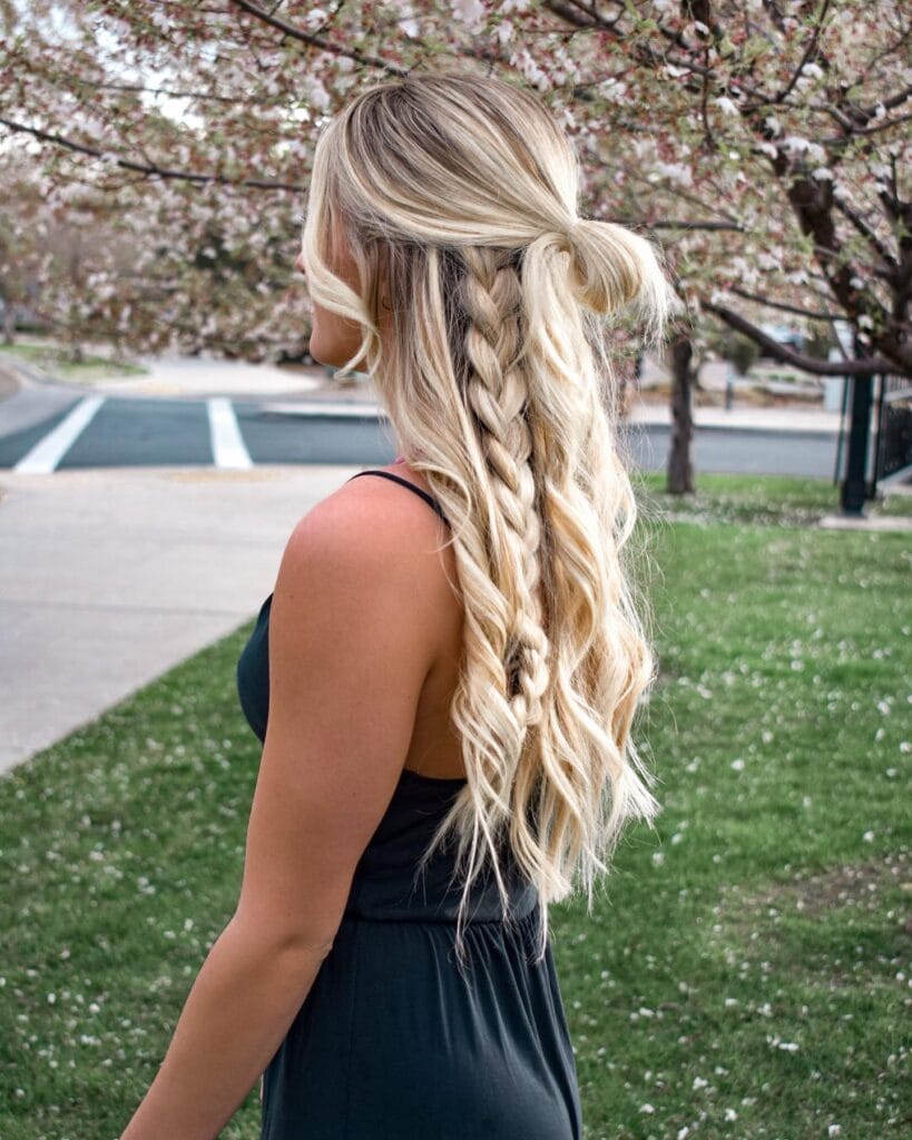 A woman from behind showing a half up messy bun with blonde waves and thick braided sections.