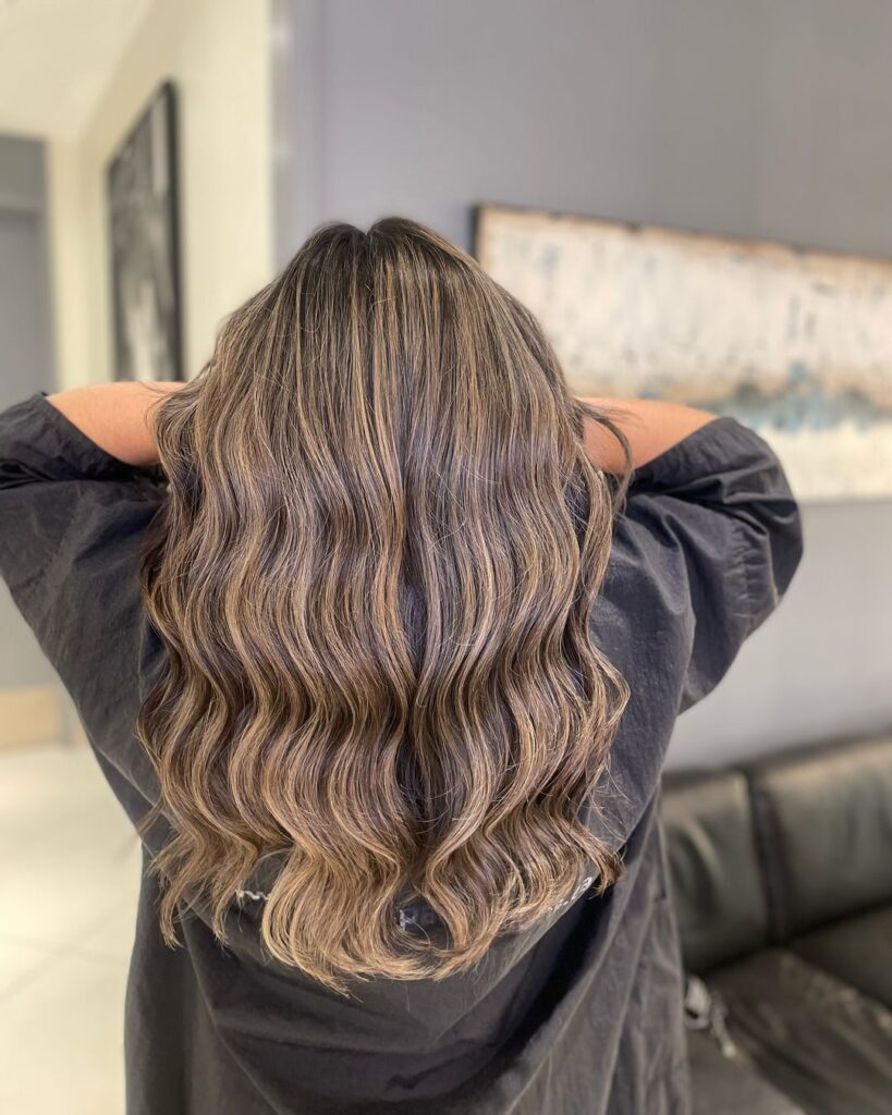 Long brunette wavy hair with soft beige highlights and natural flowing waves from the back.