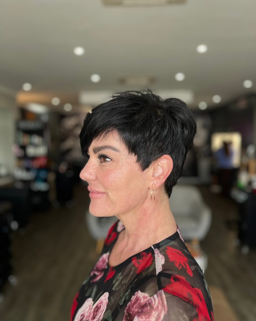 A woman with a sleek inky black pixie cut featuring a side swept fringe and tapered sides.