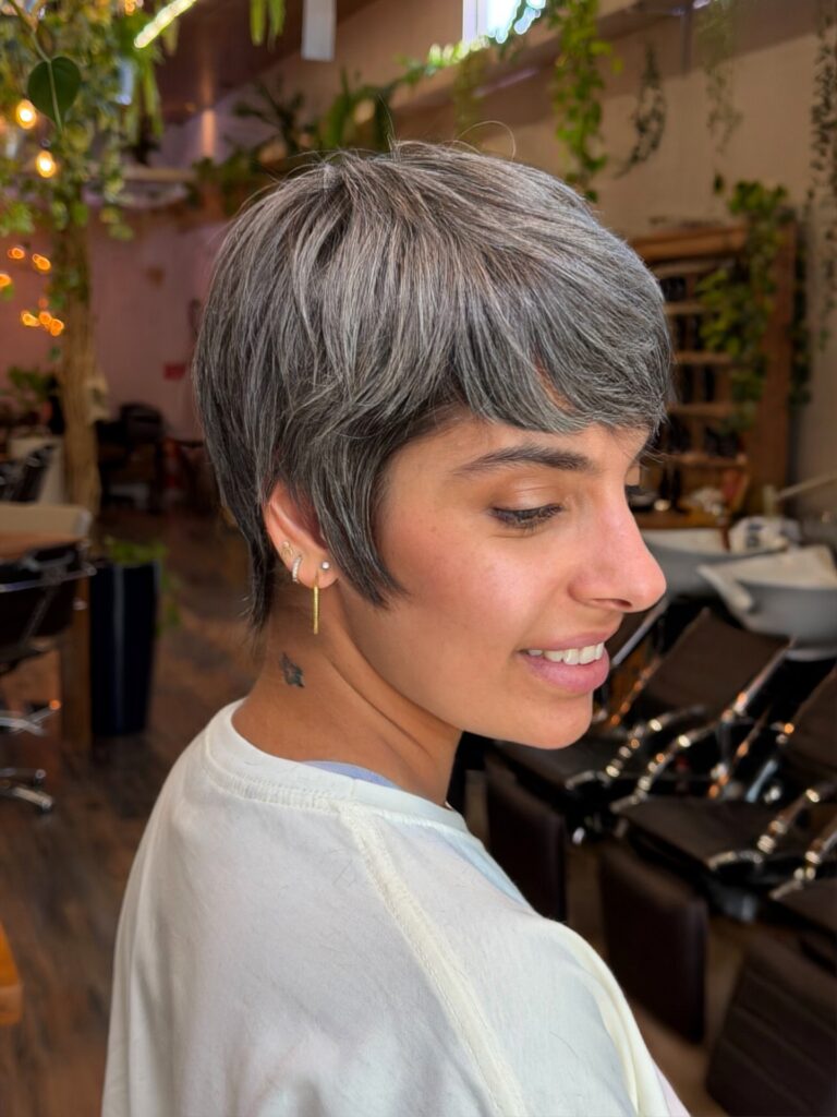 A woman with a sleek side-swept pixie cut in a natural salt and pepper silver color with soft feathered layers around the ears.