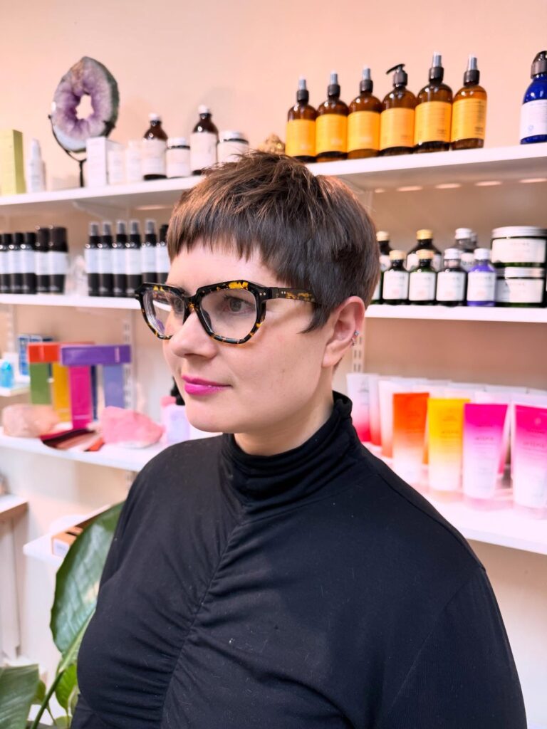 A woman wearing tortoiseshell glasses with a short choppy walnut brown pixie cut and straight blunt bangs.