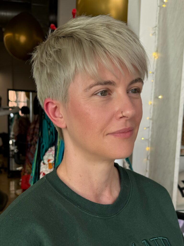 A woman with a short straight ash blonde pixie cut and a slightly textured forward swept fringe.
