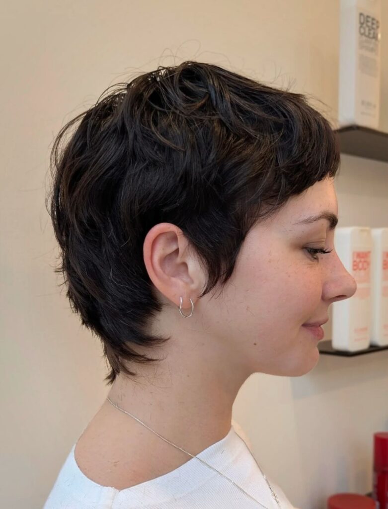 A woman with a dark brown wavy bixie cut featuring soft layers and a short wispy fringe.