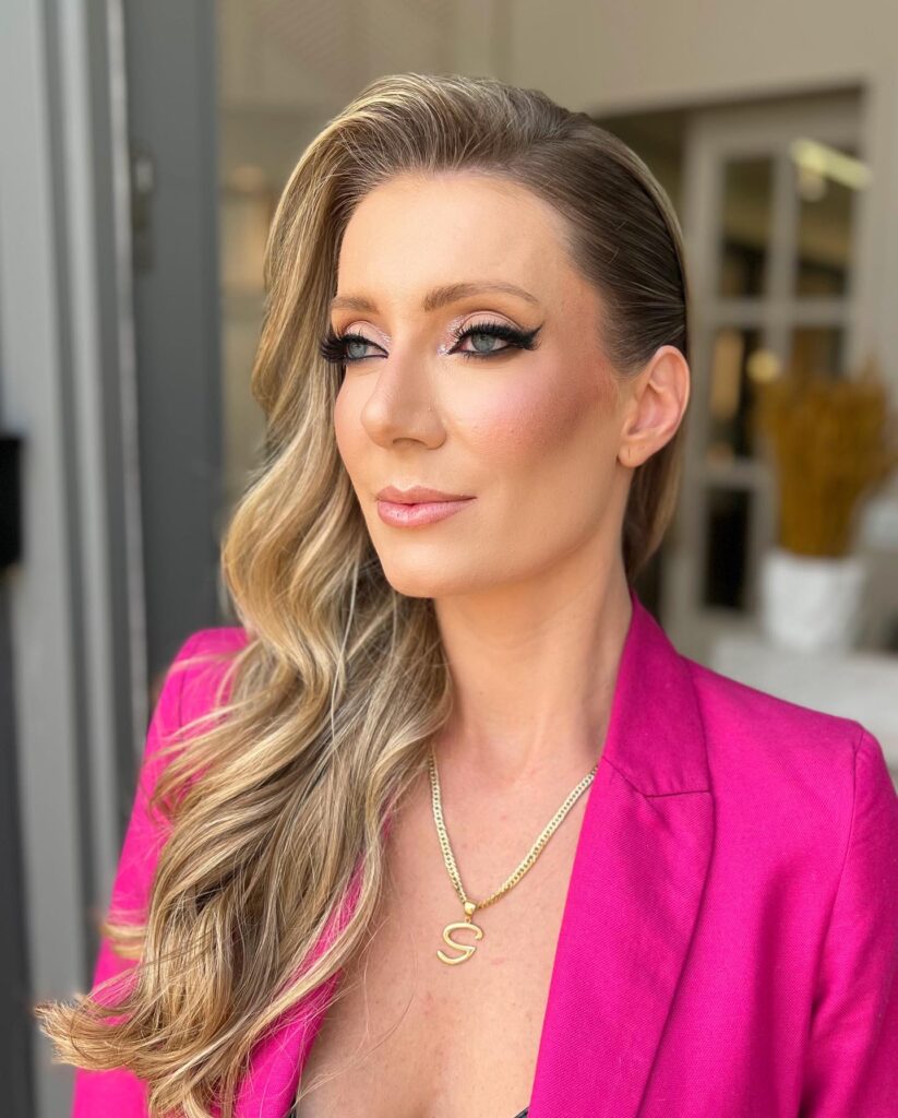 A woman with long blonde hair styled in voluminous side swept waves with one side sleekly tucked back.