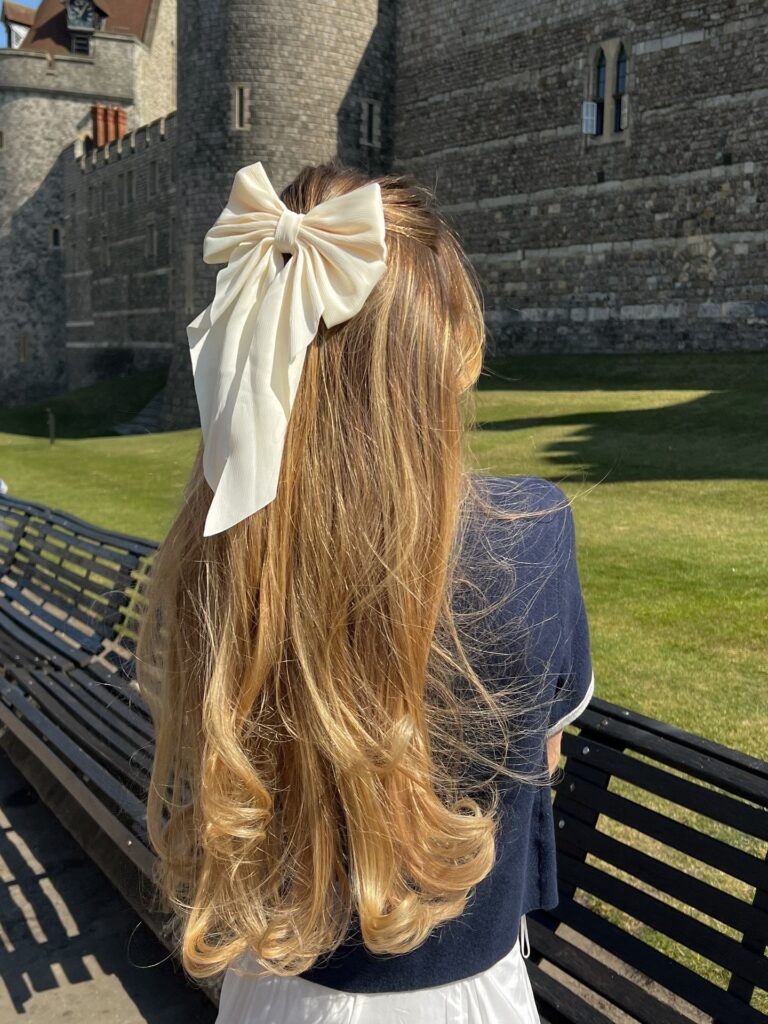 A woman with very long golden blonde hair styled in a half updo with a large cream chiffon bow and soft curls at the ends.