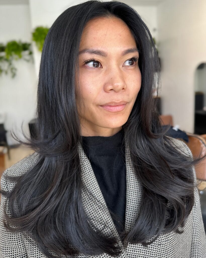 A woman with long layered dark hair styled with soft natural waves and movement.
