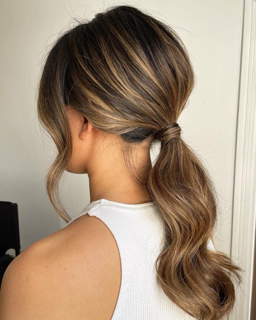 A woman with a low ponytail and soft face framing strands with loose wavy texture.