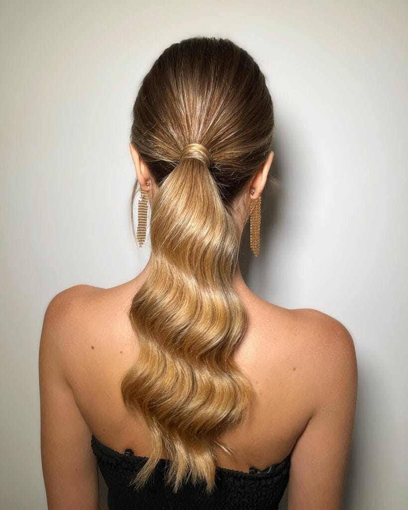 A woman with long smooth hair styled in a sleek low ponytail with soft wavy ends.