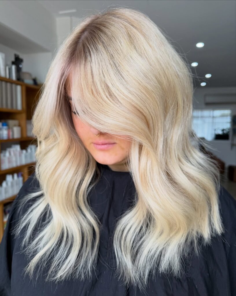 A woman with mid length platinum blonde hair styled in loose waves with heavy side swept bangs.