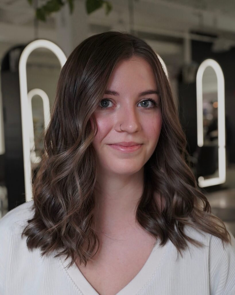 A woman with medium length dark brown hair styled in soft voluminous waves with a side part.